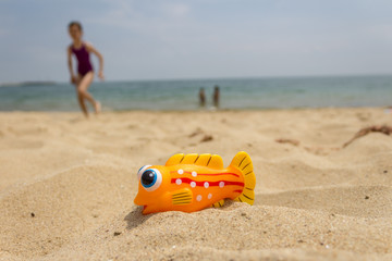 Yellow rubber toy fish on sand beach at the seaside and kids playing in the sea in background.