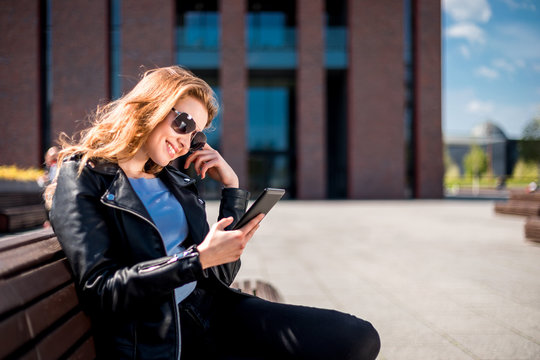 Woman sitting on bench among urban space and reading ebook using digital reader