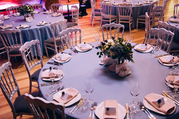 Beautiful decorated elegant wedding table for dinner with floral white bouquets, candlesticks and a white tablecloth glasses and porcelain plates