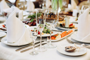 Beautiful decorated elegant wedding table for dinner with floral white bouquets, candlesticks and a white tablecloth glasses and porcelain plates