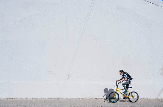 Cute little boy is riding a bike. A concrete white wall background