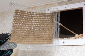 repair service man removing a dirty air filter on a house so he can replace it with a new clean. Extremely dirty and dusty white plastic ventilation air grille at home close up, harmful for health 