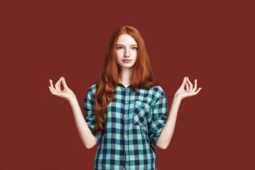 Trying to calm down. Smiling beautiful redhead girl meditating in studio. No stress concept