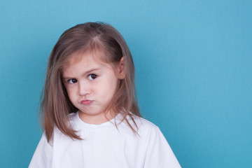 The little girl on a blue background was offended by folding her arms and frowning eyebrows