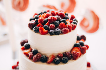 Beautiful cake covered with icing cream, summer berries on the top. Style and food photography