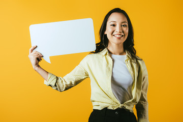 Obraz na płótnie Canvas smiling asian girl holding speech bubble, isolated on yellow