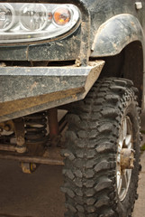 Fototapeta na wymiar Wheels, lights and bumper are laced in a swamp. Dirty truck parts close up.