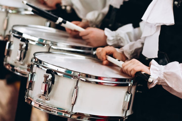 A closeup of the hands of a drummer at a parade. Children's ensemble in white shirts. White new...