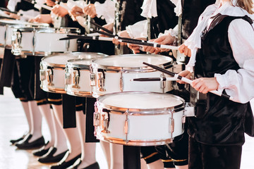 A closeup of the hands of a drummer at a parade. Children's ensemble in white shirts. White new snare drum, white sticks. The concept of a military parade and march.