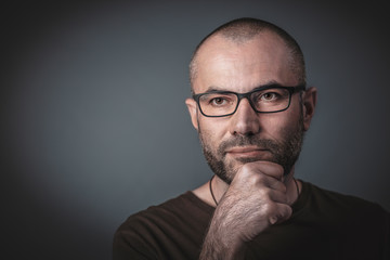 Portrait of man with glasses and hand on chin.
