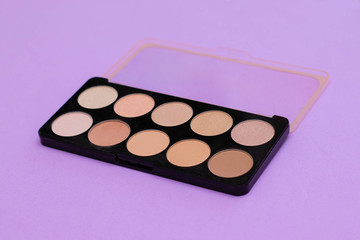 Palette with beige tone makeup on lilac background