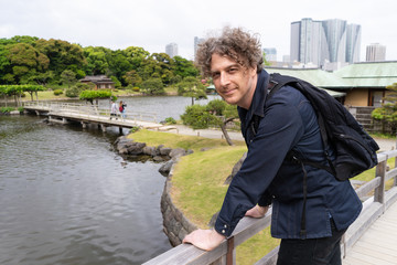 A man in his forties travels to Tokyo, Japan and visits a beautiful Japanese garden, with the city skyline behind.