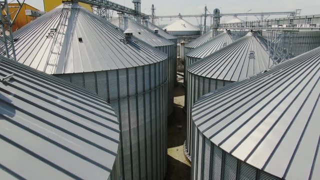 Flying slowly past tops of metal industrial conical silos standing close to each other with no people in view