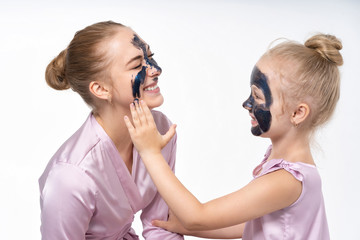 little daughter makes her mother a cosmetic mask on her face. Daughter cares, helps mom. Little daughter and young mother.