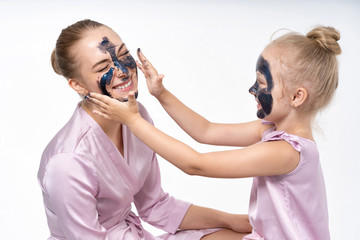 little daughter makes her mother a cosmetic mask on her face. Daughter cares, helps mom. Little daughter and young mother.
