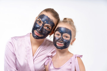 A young mother and a young daughter are sitting next to her in face masks. Facial skin care.