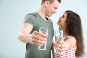 Young couple with glasses of water on light background