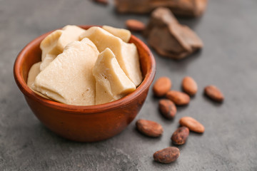Bowl with cocoa butter on grey background