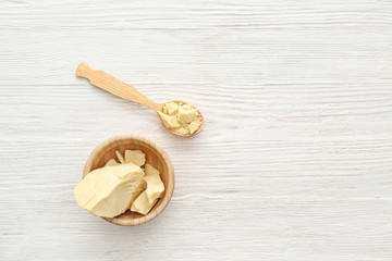 Bowl and spoon with cocoa butter on white wooden table