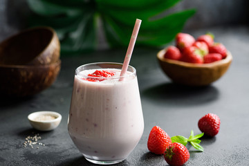 Strawberry coconut smoothie or milkshake in glass with drinking straw on black background