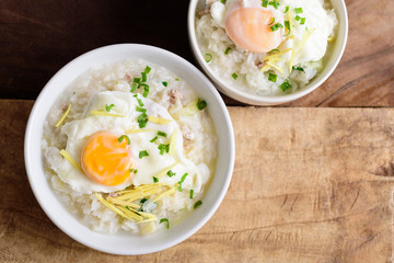 Thai rice soup or soft-boiled rice with pork and egg in the bowl on wooden background, top view