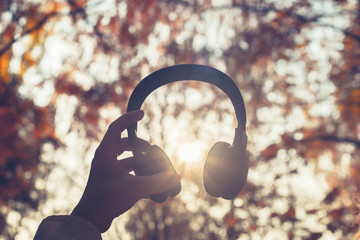 Female with headphones walking on the park listen sounds or music of autumn forest. Concept. Indian summer season