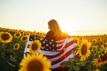 Beautiful girl with the American flag in a sunflower field. 4th of July. Fourth of July. Freedom....