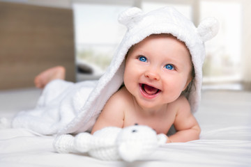 Happy six month old baby with a hooded towel lying on a bed and having fun