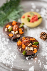 Christmas theme. Handmade chocolates candy. Mini chocolate dessert covered with nuts and dried fruits. Garland lamps bokeh on background. Copy space