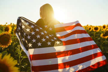 Beautiful girl with the American flag in a sunflower field. 4th of July. Fourth of July. Freedom....