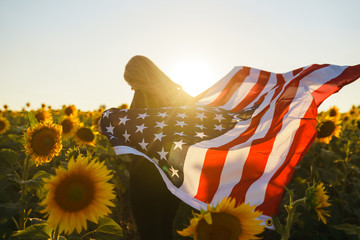 Beautiful girl with the American flag in a sunflower field. 4th of July. Fourth of July. Freedom....