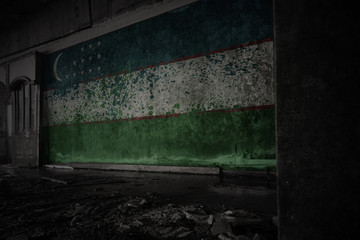 painted flag of uzbekistan on the dirty old wall in an abandoned ruined house.