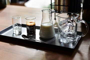 iced coffee latte, ice cubes espresso milk and sweet syrup served in various test tubes on wooden table in morning cafe, selective focus
