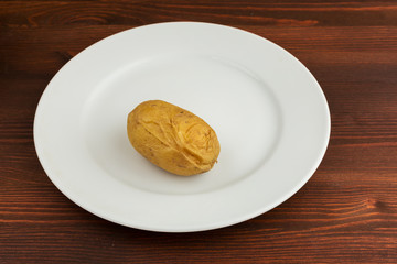 Potatoes boiled in their skins lie on a white round plate on a wooden brown table.