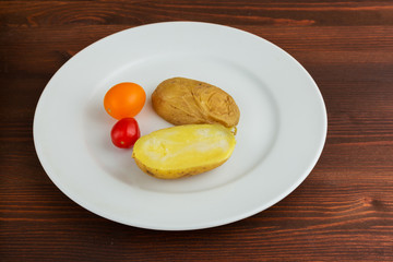 Slices of boiled potatoes and two tomatoes lie on a white round plate on a wooden brown table.