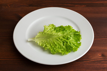Slices of boiled potatoes, two tomatoes and a leaf of parsley, lie on a white round plate on a wooden brown table.
