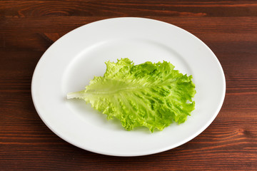 Slices of boiled potatoes, two tomatoes and a leaf of parsley, lie on a white round plate on a wooden brown table.