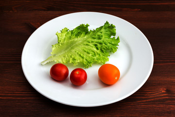 Green leaf lettuce and tomatoes on a white plate on a wooden table.