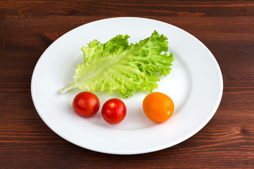 Green leaf lettuce and tomatoes on a white plate on a wooden table.