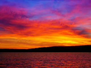 Bright colorful sunset over a lake. Beautiful reflection by a tranquil water of amazing sky and the lakeside at sundown in the summer evening. Lake Elovoe (Spruce Lake), South Ural, Russia.