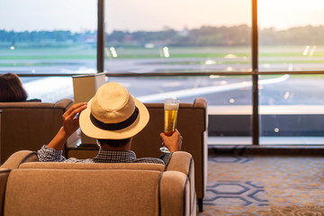 man traveler with hat holding beer glass and looking to airplane, Asian passenger sitting and relax...