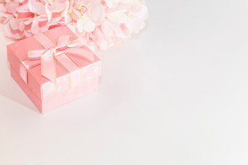 Festive background for a greeting card with a pink gift box with a bow and flowers of artificial hydrangea in pastel colors on a white background with a copy space