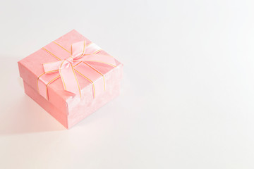 Festive background with gift wrap with a box of pink color with a bow in pastel colors on a white background with copy space