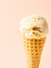 Scoop of delicious salted caramel toffee vanilla ice cream in waffle cone on pastel peachy pink background. Summer desserts sugar addiction indulgence concept. Recipe cafe menu template