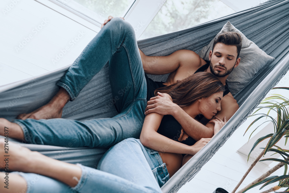 Wall mural Loving couple. Top view of beautiful young couple embracing while sleeping in the hammock indoors