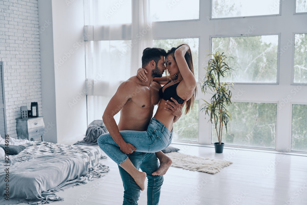 Wall mural pure feelings. handsome young shirtless man carrying semi-dressed attractive woman while standing in - Wall murals