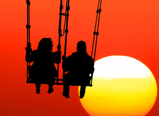 Couple (silhouettes of woman and man) on a seesaw swinging and flying high to sunset. Huge yellow sun disk on a red sky Inspiration, love and dreams