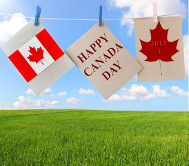 Happy Canada Day. Holiday greeting cards with Maple leaf and Canadian flag. Signs hanging on rope against beautiful Canadian landscape of wonderful green wheat field under a high and bright blue sky