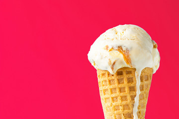Scoop of delicious melting salted caramel toffee vanilla ice cream in waffle cone on coral pink...