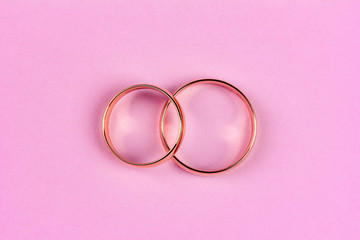 a pair of gold wedding rings on a pink background, top view flat lay